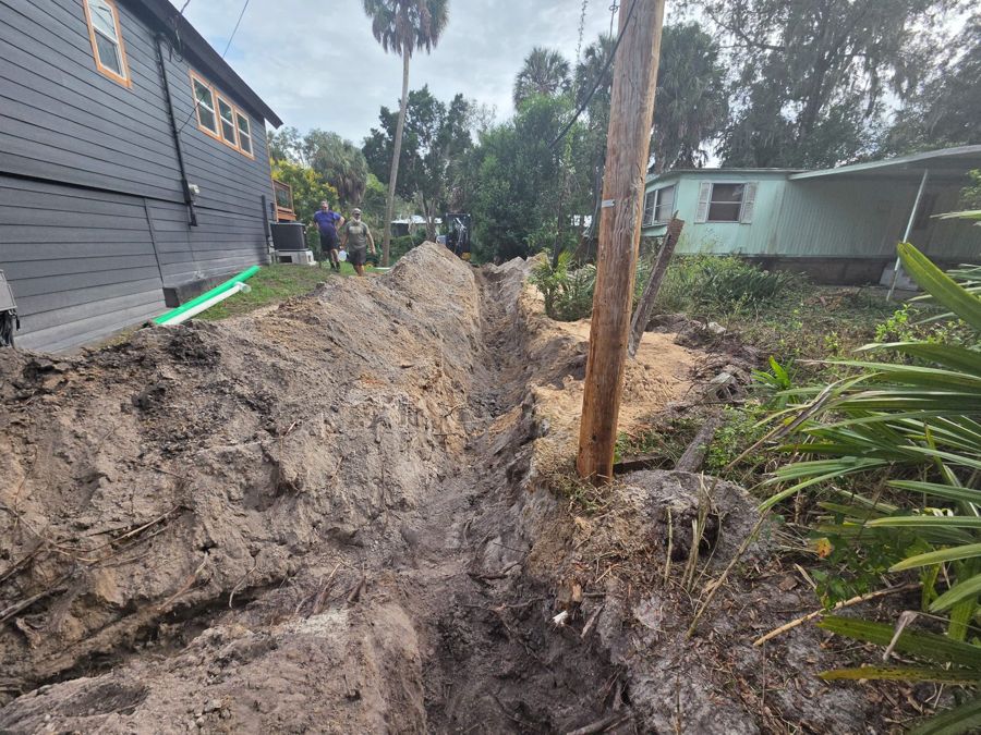 Water line trench cut alongside a house, excavator at the far end